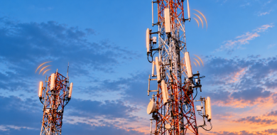 Two telecom towers with orange wireless signal indicators against a blue evening sky.