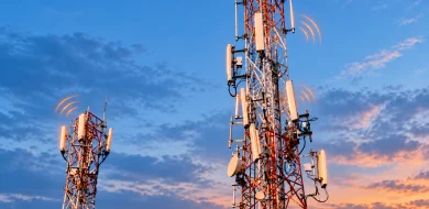 Two telecom towers with orange wireless signal indicators against a blue evening sky.